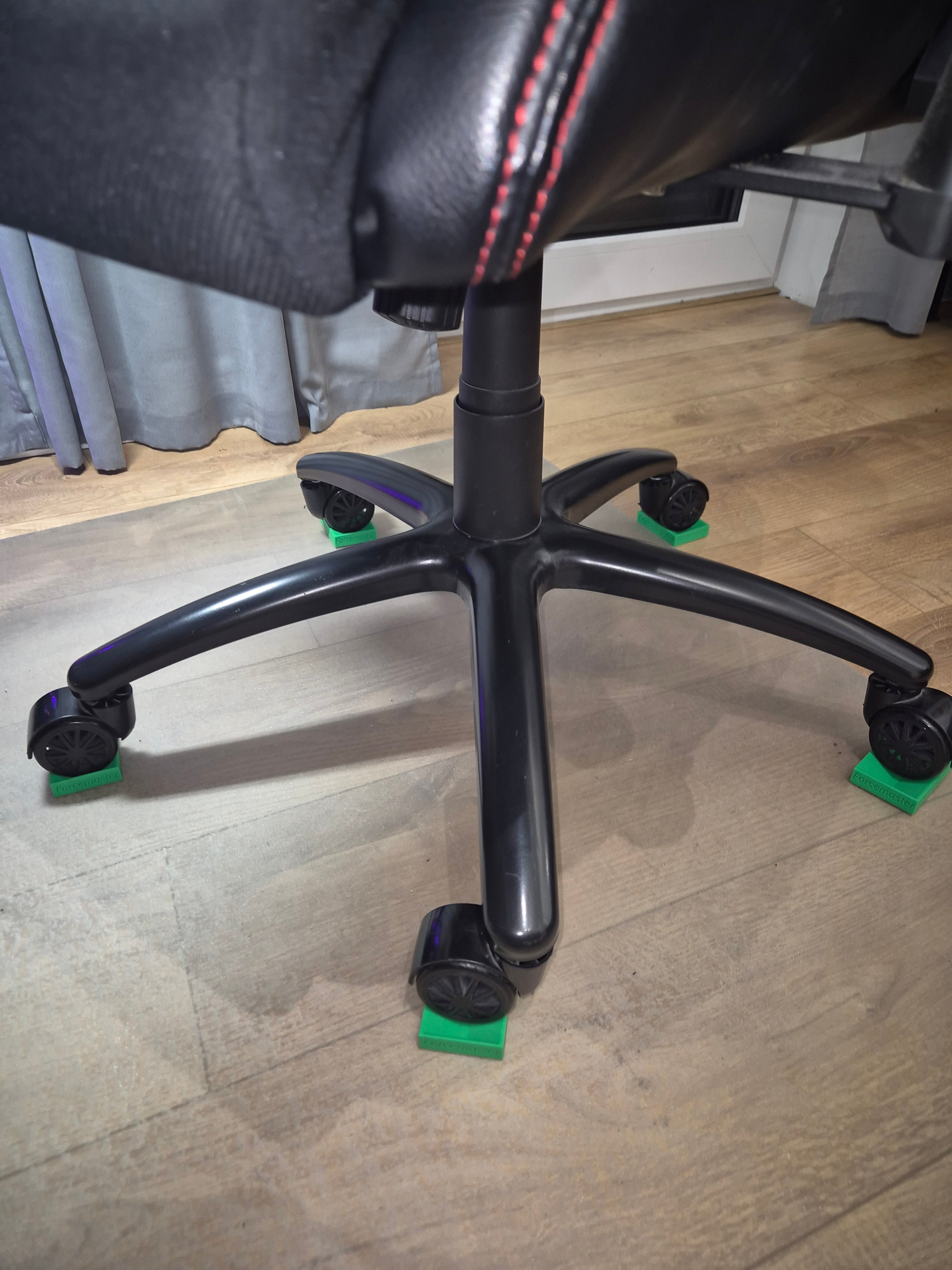 Komplet 5 sztuk zielonych blokad Forcemaster zamontowanych pod wszystkimi kółkami czarnego fotele obrotowego na jasnej podłodze.