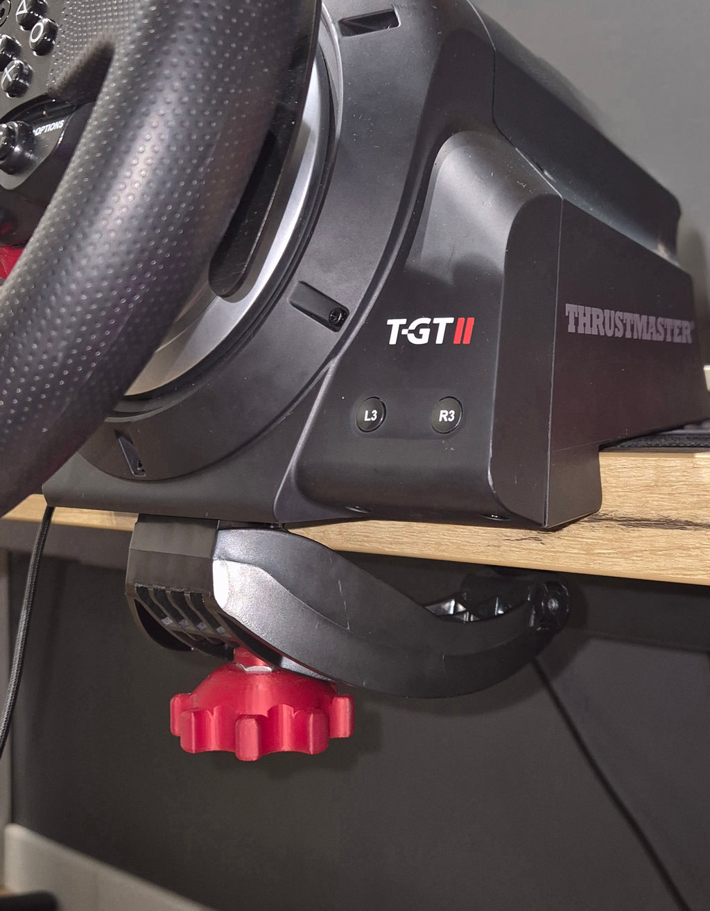 Czerwona śruba Forcemaster wkręcona w bazę kierownicy Thrustmaster zamontowaną do blatu biurka, zapewniająca stabilność podczas jazdy.
