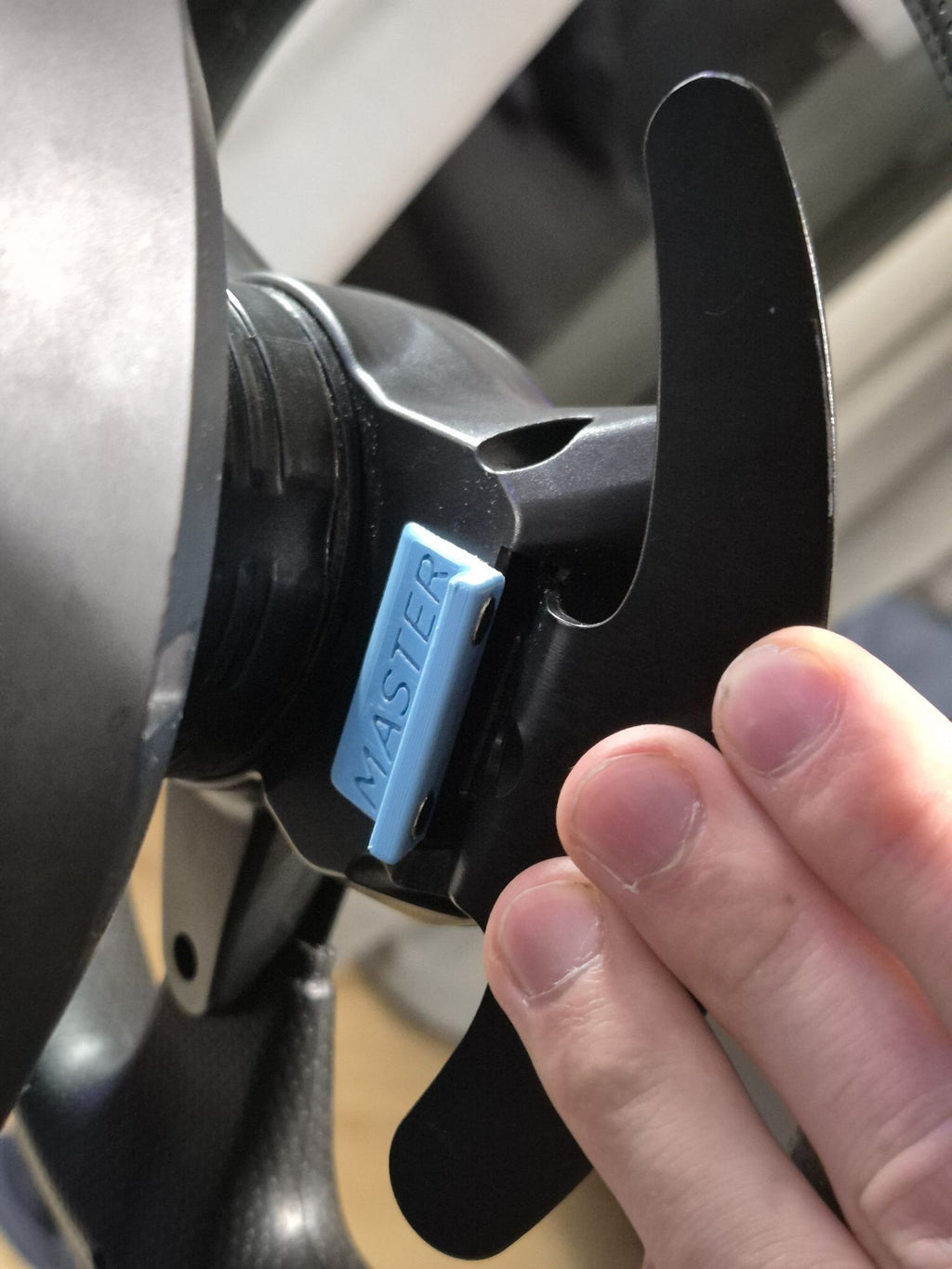 Detal niebieskiego modu Forcemaster wykonanego w technologii druku 3D, zamontowanego na kierownicy gamingowej.